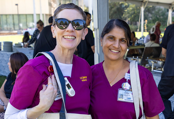 Three UC Davis Health employees in teal scrubs smile together outdoors.