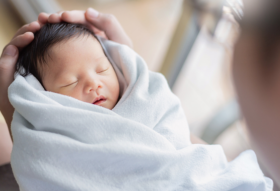 A newborn wrapped in a white blanket rests in someone's arms.