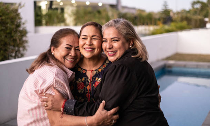 three women smiling and hugging each other in front of a pool