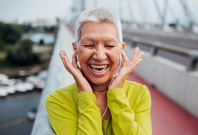 A woman smiling and holding headphones into her ear.
