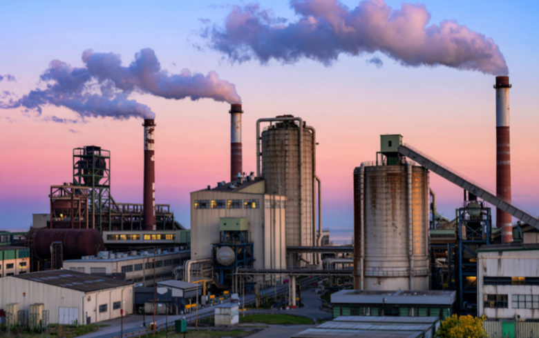 Sunset with factory buildings releasing pollution into the environment.