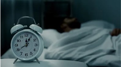 man sleeping in dark room with alarm clock that is visible 