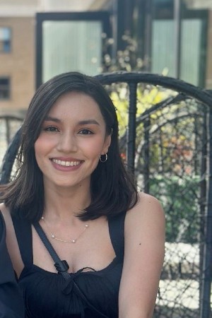 Headshot of Itzel smiling while sitting on black outdoor chair
