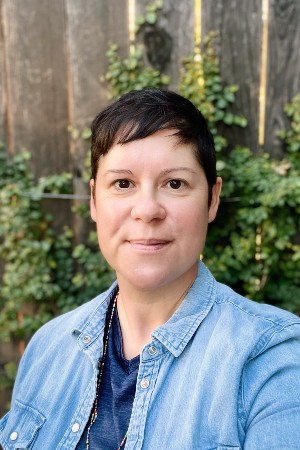Headshot of Jeannette smiling in front of plant vine that is climbing on fence