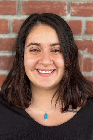 Headshot of Magaly smiling in front of red brick wall