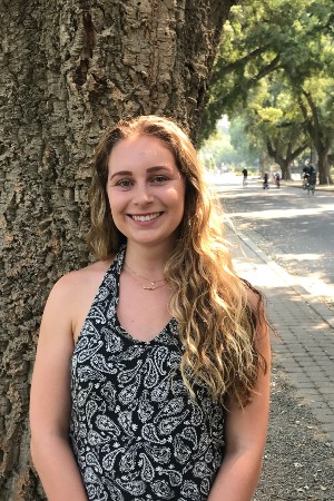 Tessa smiling in front of a tree and paved walkway