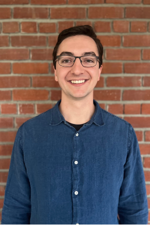 Headshot of Tyler smiling in front of red brick wall