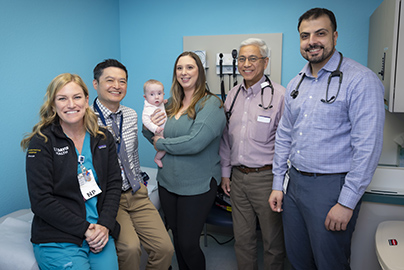 Mother holding her baby next to pediatric cardiology team members
