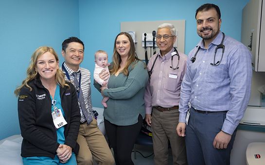Mother holding her baby next to pediatric cardiology team members