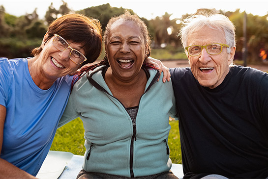 Three older adults with their arms around a each sitting at a park.