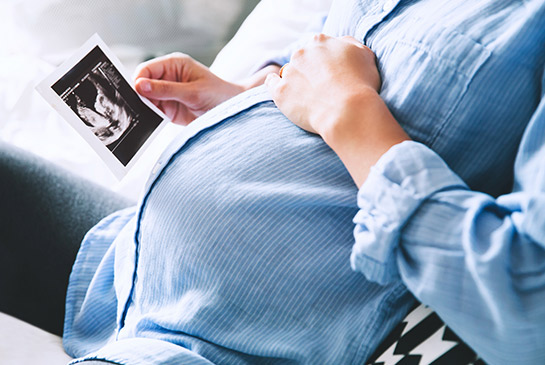 Pregnant woman holding ultrasound printed image.