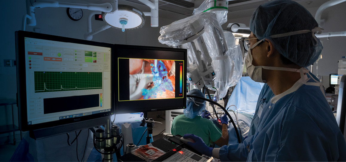 A cancer specialist in the operating room looking at a patient scan on a monitor.