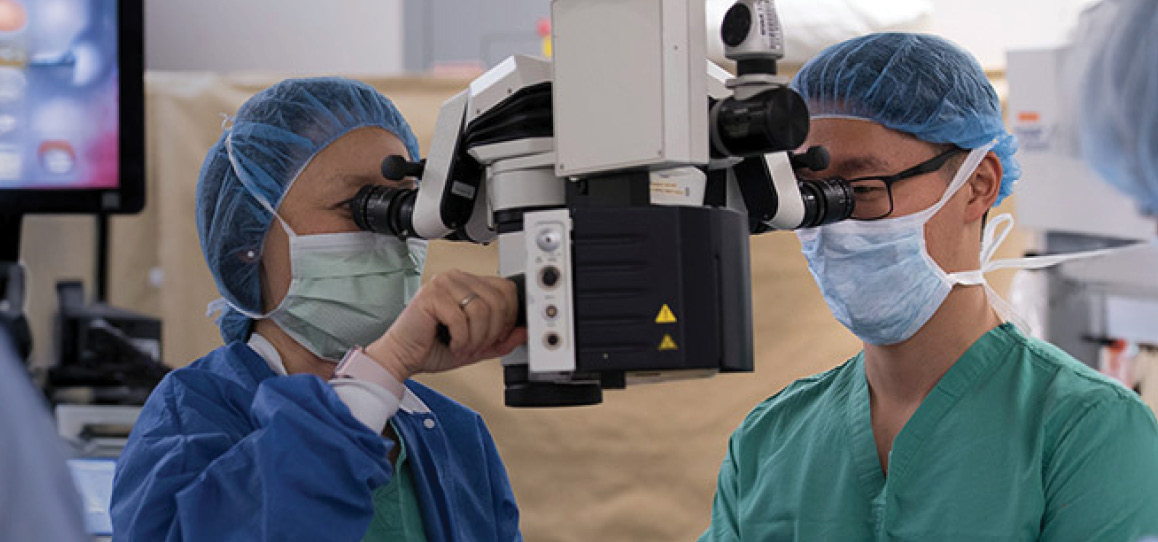 Two eye care specialists using a magnifying device during a patient procedure.