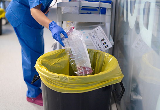 nurse wearing gloves disposing of medical waste in designated bin