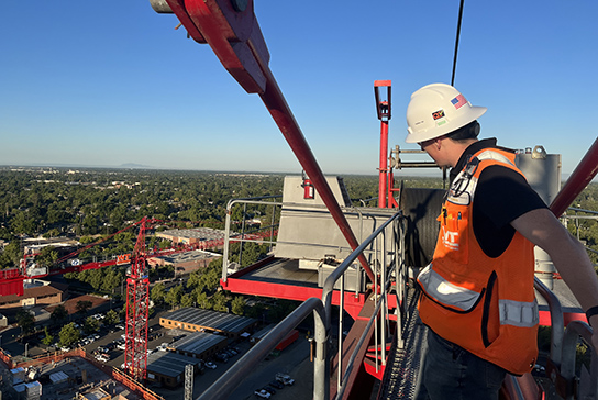 Construction worker on the top of a crane, looking down on a construction project below.