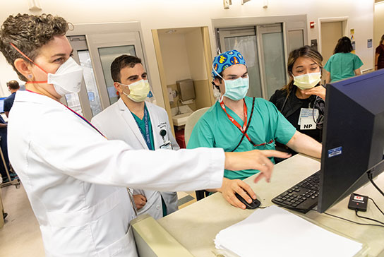Four medical professionals wearing protective masks, looking at a computer monitor.