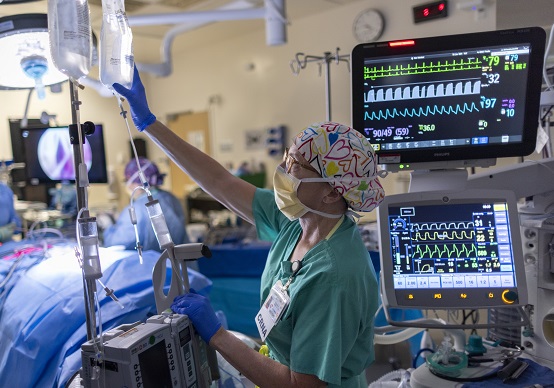 CRNA working with medical equipment and monitors in surgery room.