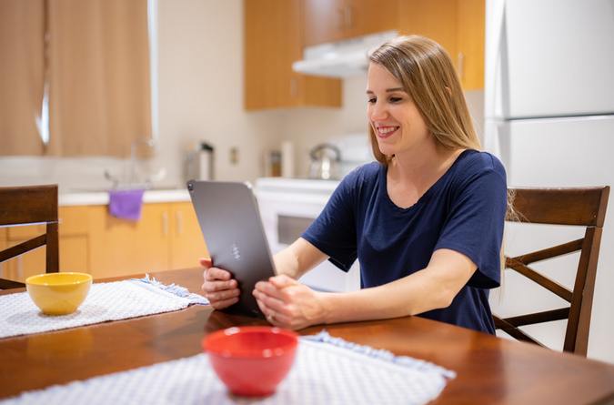 A smiling woman uses her tablet device at her kitchen table 