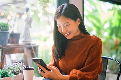 A smiling woman interacts with a telehealth video visit on a phone screen from her garden