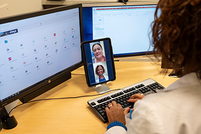 A health provider types while on a telehealth video visit, with patient on split screen