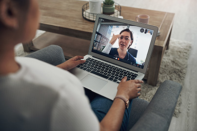 A health provider appears on a patient's laptop during a telehealth video visit from a living room chair