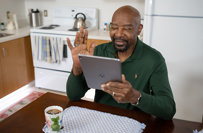 A man in his home waves to a hospitalized family member on a tablet device