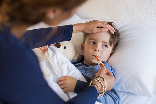 A young boy gets his temperature taken in bed
