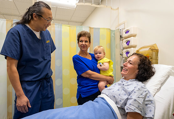 A hospitalized patient talks from her bed with a nurse and visitors 