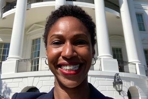 A woman in a professional blue jacket takes a selfie in front of the White House