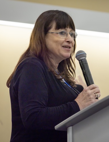 professional woman stands at podium, holding a microphone