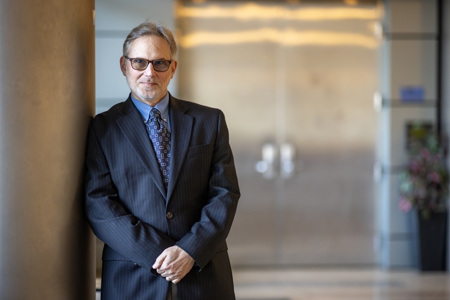 professional man in suit stands in wide hallway, leaning against the wall