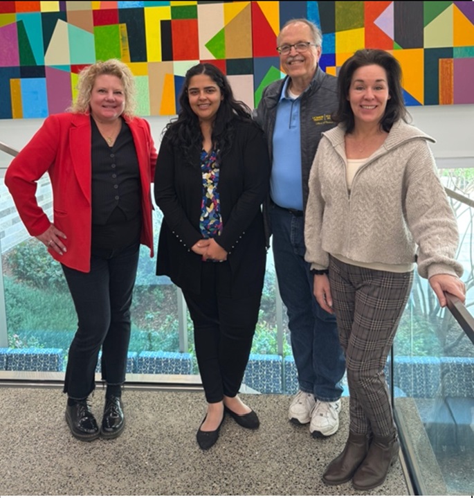 four professionals standing in front of a mural composed of brightly colored geometric shapes