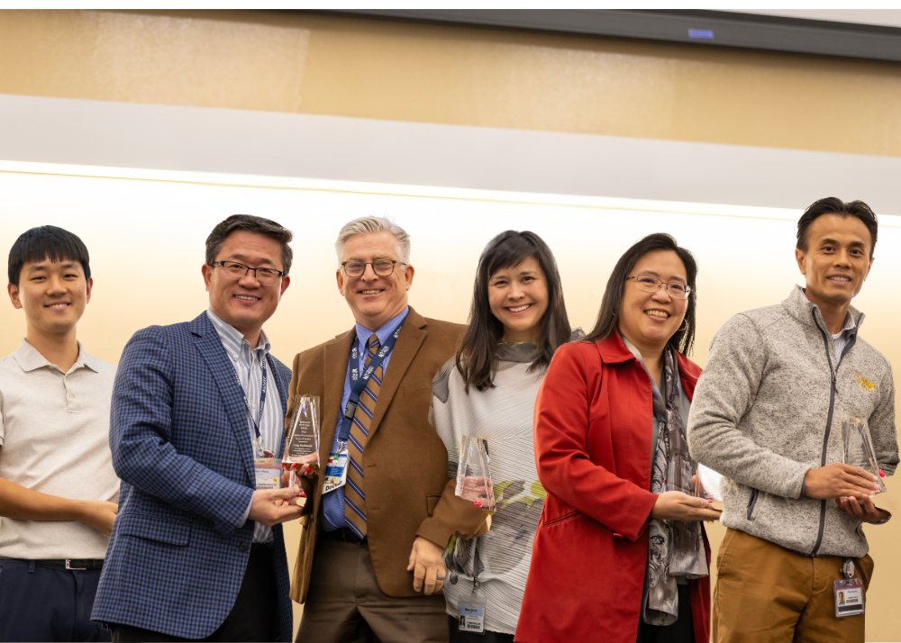 Six individuals holding award trophies on a stage