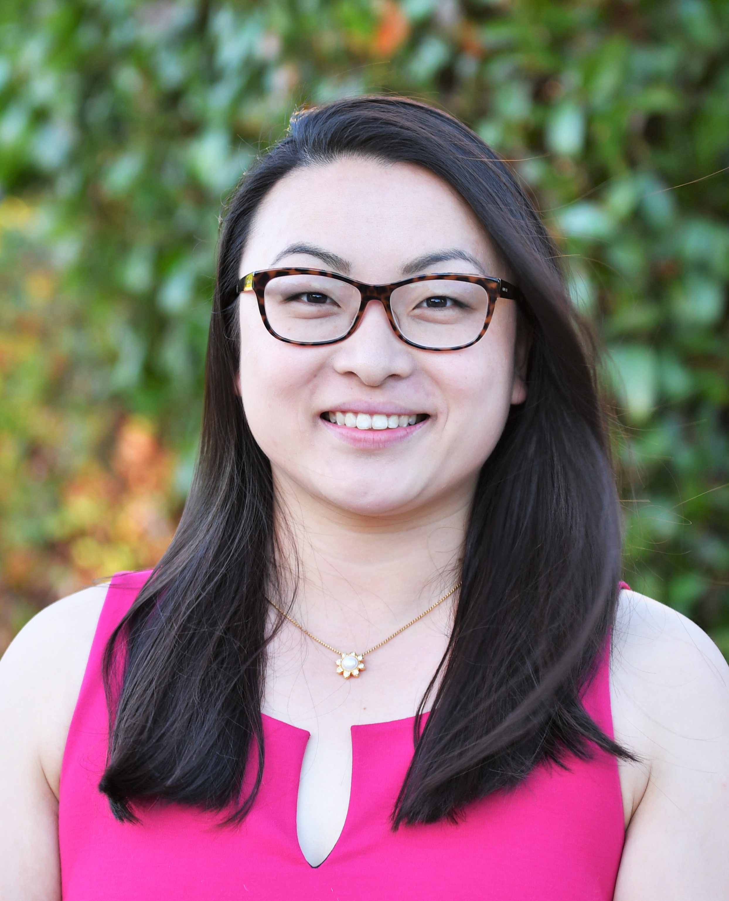 headshot of professional woman with dark hair, glasses and a pink top