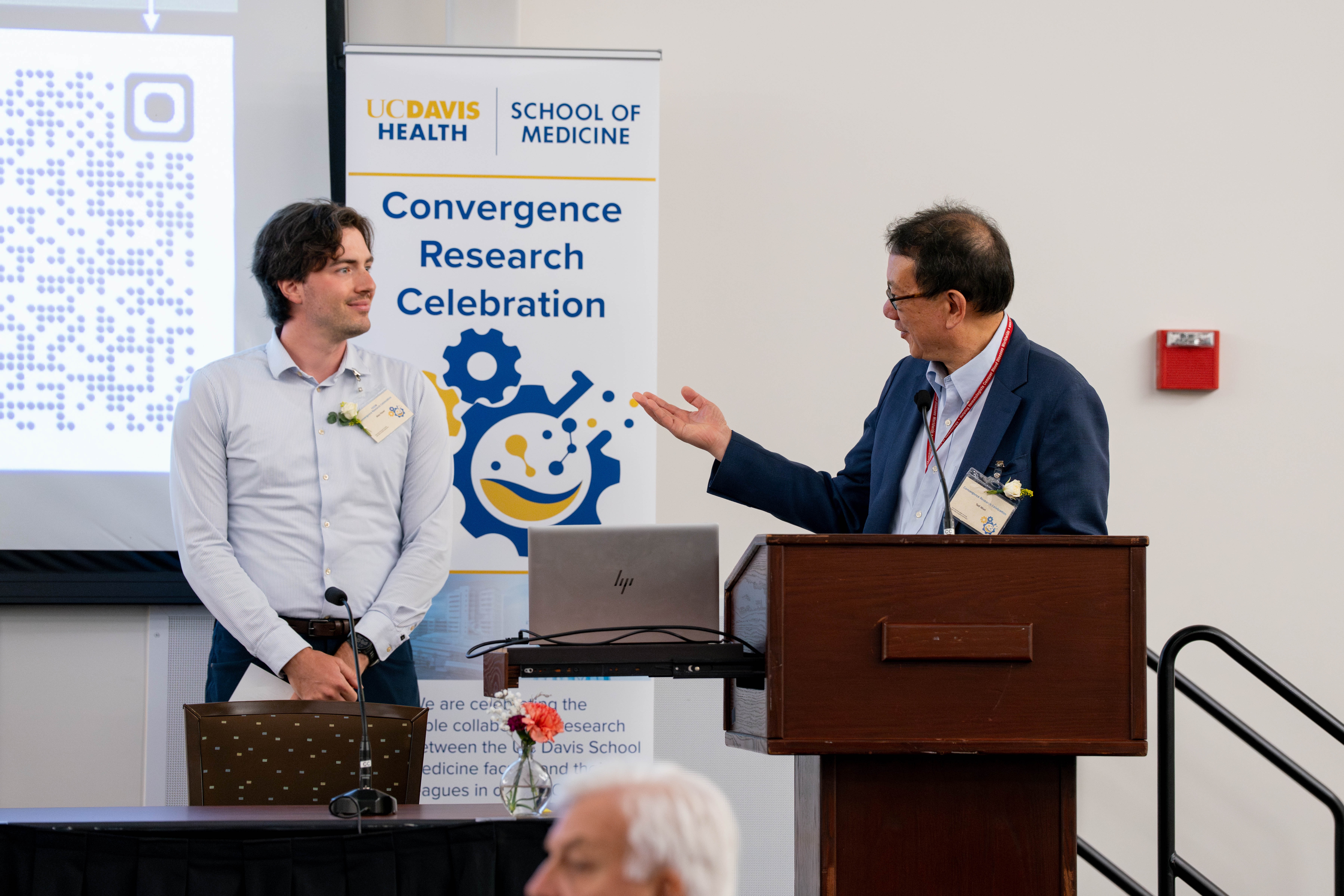 A professional man behind a podium smiles at a man on stage