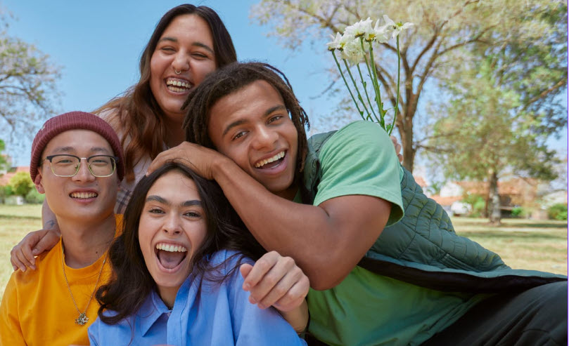 stock photo of four young adults gathered together outside on a sunny day, smiling