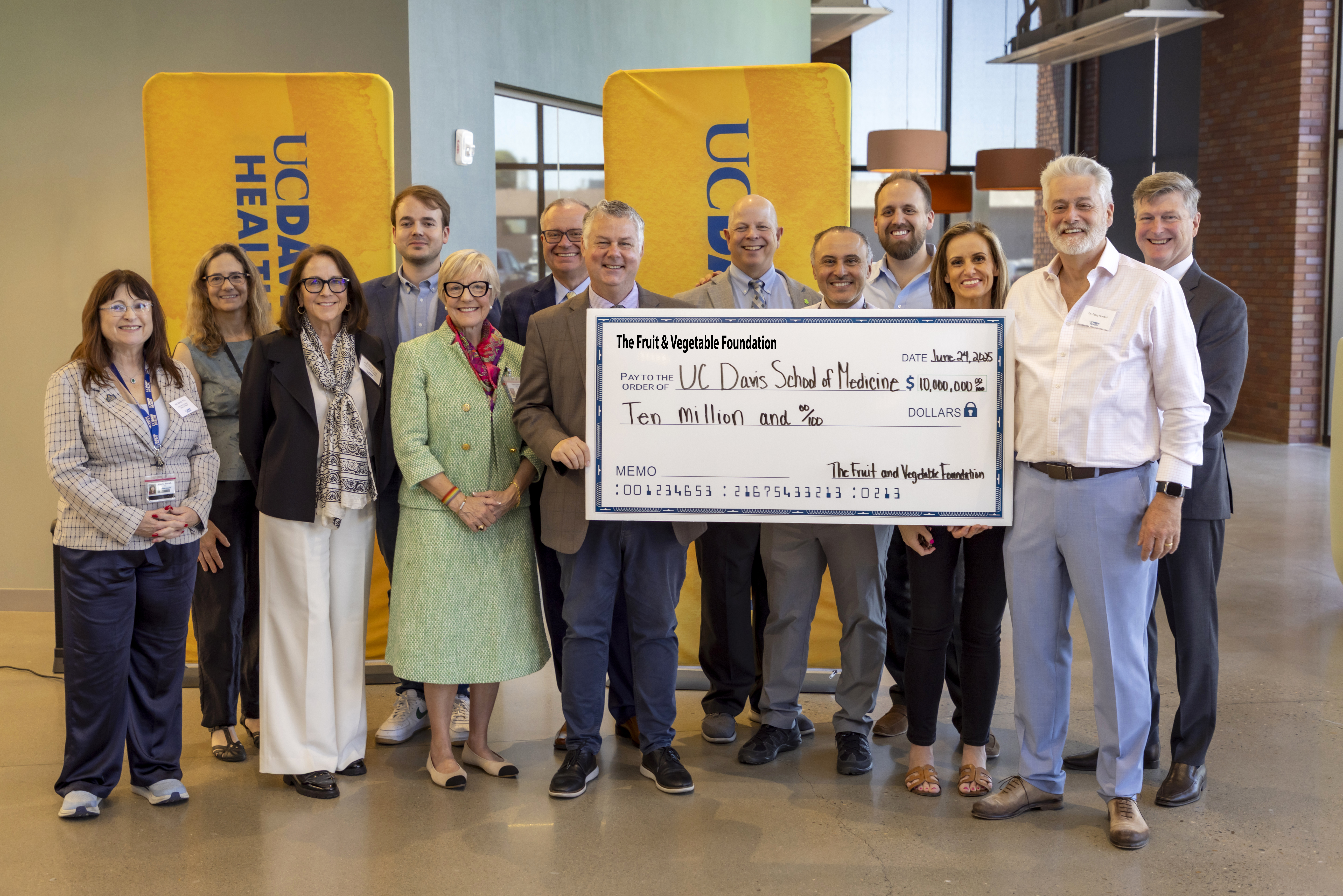 a group of people pose around and hold up a large novelty check that represents a ten million dollar donation