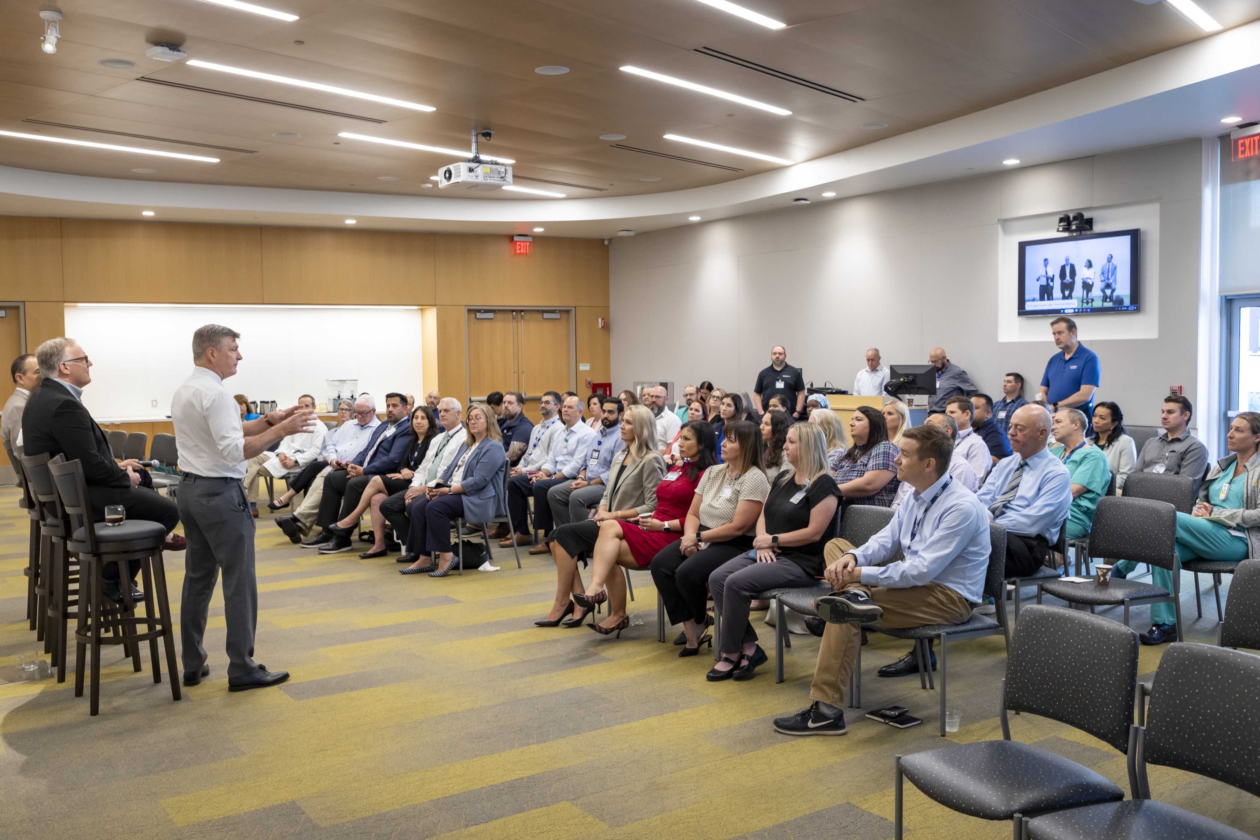 a large group gathers in a lecture hall to listen to several speakers
