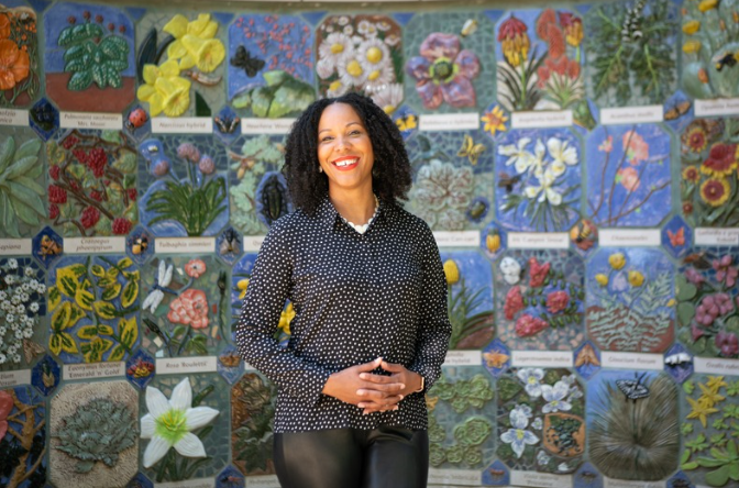 a woman in a dark shirt and pants stands in front of a mural of flowers