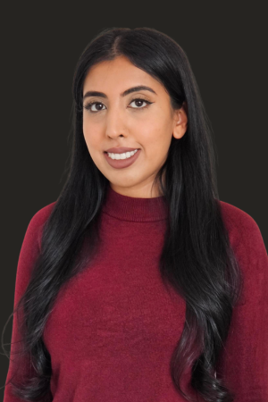 Headshot of Ashley Balley. Woman is wearing a dark red top against a gray background. 