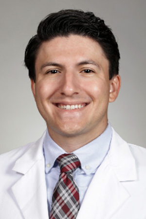 Portrait of medical student Aaron Vaughn-Martinez in white coat and smiling