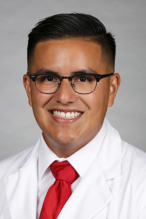 Portrait of medical student Carlos Melchor in white coat and smiling