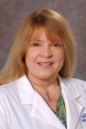 Studio portrait of Jan Nolta wearing a white UC Davis Health lab coat over a patterned blouse, photographed against a neutral backdrop.