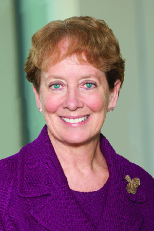Formal painted portrait of Julie Frieschlag wearing a blue suit, seated with hands resting on a table, campus landscape and sky in the background.