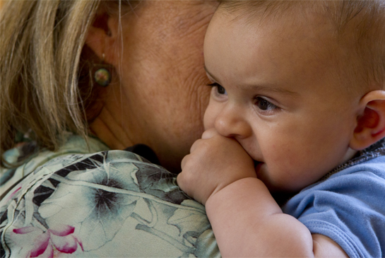 A baby being held by an adult, sucking on their hand