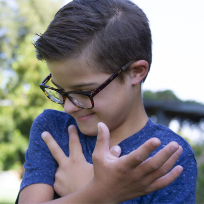 A child wearing glasses, looking down with their arms crossed