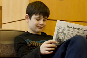 A child sitting on a chair and reading a newspaper