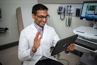 smiling clinician waves to his screen during a Telehealth Express Care visit
