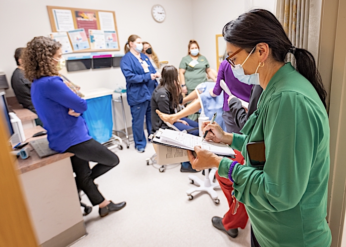 doctors working in exam room as a woman looks on taking notes
