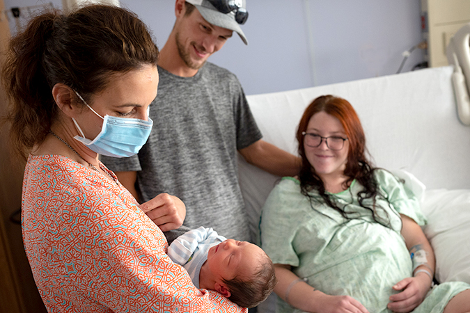 Obgyn doctor holding baby, with baby's family in hospital room